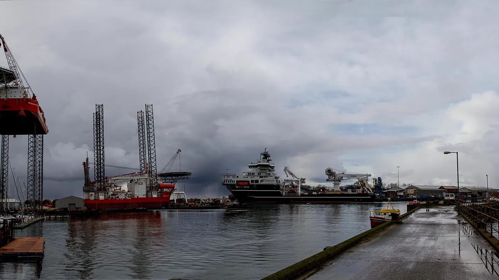 Jack-up installation vessels and an offshore support ship alongside under a storm sky
